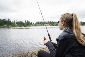   Teenage girl fishing in a lake while sitting on a dock