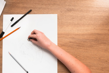 From above hand of a person applying rubber on a draw. Horizontal indoors shot. Drawing lessons, art school, young artist concept