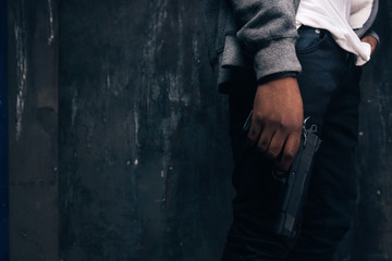 Unrecognizable armed black rapist closeup studio shoot. Gangster man with gun in hand on dark...
