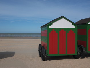 Cabines de plage sur le sable, rouge et verte, ciel bleu.