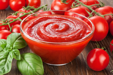 Bowl with ketchup basil and tomatoes on a wooden background.