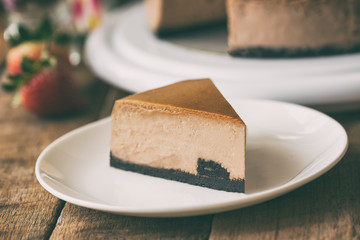 Homemade chocolate cheesecake on rustic wood table.Baked chocolate cheesecake on plate.Brownie cheesecake for coffee break or tea time in cafe.Triangle slice piece of chocolate cake in dramatic style.