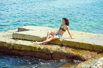 Model posing against the sea in a swimsuit , the young woman resting on the sea