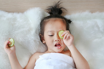 Cute little Child girl with a slice of cucumber in her eye.