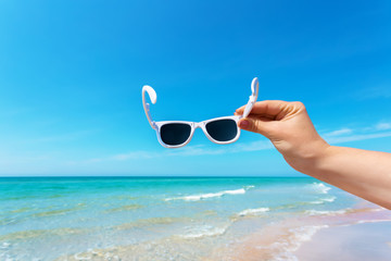 Sunglasses in hand on background of the beach