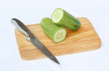 Cucumber slices on wood block with knife against white background.