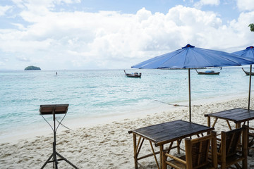 holiday and relaxation concept - bamboo table and chair at the seaside with blue parasol
