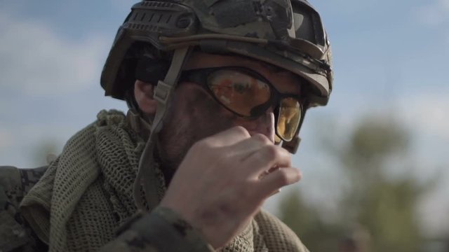 Slow motion, close view, soldier on battlefield having a smoke while other soldiers talking at background