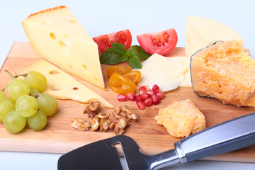 Assortment of cheese with fruits, grapes, nuts and cheese knife on a wooden serving tray.