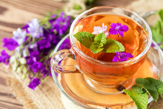 Glass cup of summer herbal tea with fresh mint and field larkspur. Wooden table. Shallow depth of field.