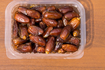Dried date fruits in plastic container on wooden table. Top view