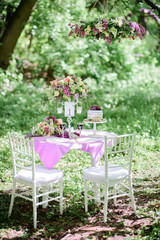 Table number one with bouquet of violet flowers and little cake on it stands in the garden