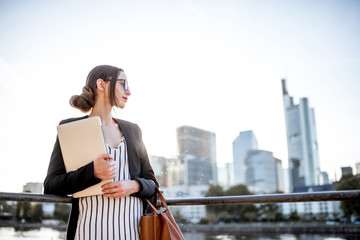 Young businesswoman having a coffee break outdoors sitting on the bridge in Frankfurt city during the sunset