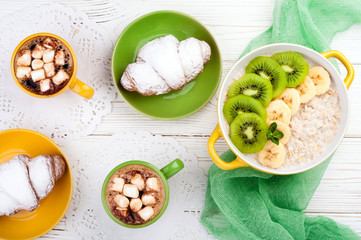 Breakfast with oatmeal porridge, croissant, fruits and coffee cup. Oatmeal with kiwi and banana. Healthy breakfast and meal concept. Top view