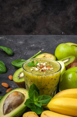 Healthy green smoothie and ingredients on dark background. Kiwi smoothie with fruits and almond nuts. Superfoods, diet, detox, health, vegetarian food concept