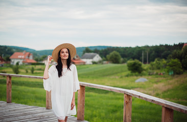 Brunette woman in hay hat walks on the balcony over green field