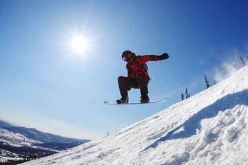 Naklejka na ściany i meble Snowboarder jumping from the springboard against the sky