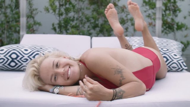 Happy young woman in red bathing suit smiling while lying on the bed