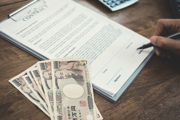 Fototapeta premium Businessman signing contract with money, Japanese yen banknotes, on the table