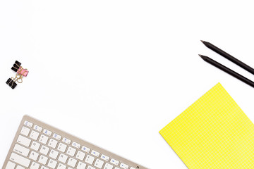 computer keyboard, a yellow pad, two black pencil and clips for paper on white background. Minimal...