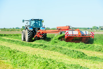 Tractor with hay mower cutting grass for hay on a field.
