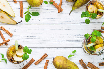 Pear, cinnamon sticks, glasses on white table. Ingredients for refreshing drink. Copy space, top...