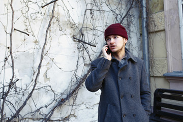 Man in red hat talks on the phone standing before the wall