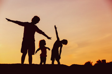 father with son and daughter silhouettes play at sunset