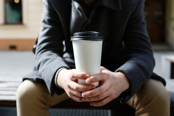 White paper cup of coffee to-go in man's arms