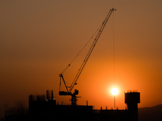Construction site with silhouettes of crane catching the sun durung  sunset.