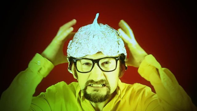 An angry man wearing a tin foil aluminium hat (believing that it shields the brain from threats such as electromagnetic fields, mind control or reading). Disturbing colored shadows on his face.
