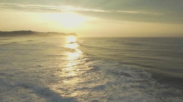 Ocean Scenic Landscape Beach Sunrise Warm. Waves Rolling and Crashing on Rocks. Slow Smooth Gliding Aerial Drone shot.