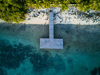 Top view aerial shot of wooden pier in tropical ocean with white sand beach, palms and blue water