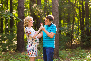 Naklejka premium Pregnancy, family, happiness and fun concept - Man and pregnant woman have fun in the park