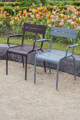 Two brown and blue street armchairs with drops of water near the flower field in bloom
