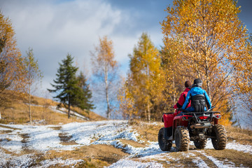 Rear view. Couple having fun on snow-covered road while driving a quad bike on a sunny day with...