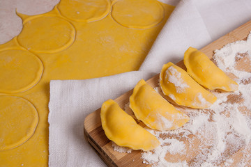 Close up view of ready for boiling vareniki, dumplings, pierogi on wooden cutting board with flour..
