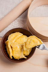 Close up view of boiled varenyky or dumpling with cottage cheese or curd on metal fork. Fresh boiled homemade ukrainian dumplings in clay bowl on wooden background..