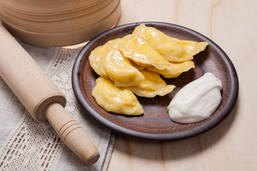 Fresh boiled varenyky or dumpling with cottage cheese or curd on clay plate and with sour cream on wooden background..