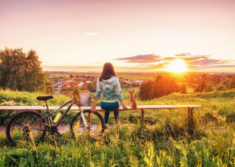 A girl and a dog are looking at a beautiful sunset on the horizon. Walking with a dog on a bike in the evening. A young girl and a dwarf chihuahua look at the setting sun in the evening.