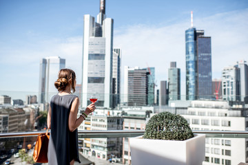 Fototapeta na wymiar Young businesswoman enjoying wine on the terrace with great view on the skyscrapers in Frankfurt city