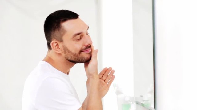 happy man applying aftershave to face at bathroom