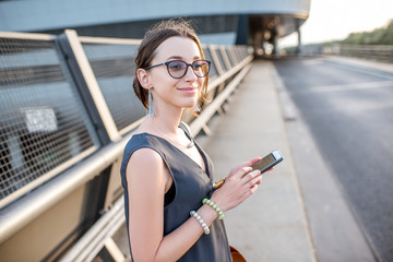 Young businesswoman standing with phone on the highway during the business trip