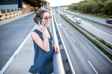 Fototapeta premium Portrait of a young businesswoman talking with phone on the highway during the business trip on the sunset