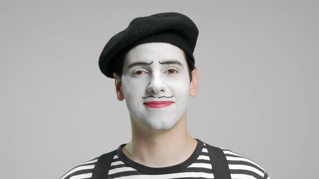 Close-up of a mime looking at the camera and smiling isolated on gray background