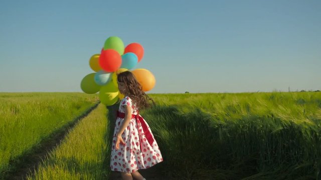 The child is spinning with balloons. A little girl with balloons on a country road.
