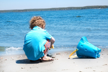 Little boy with blonde curly hair is playing at the beach. Summer break, vacation, family trip, summer beach fun