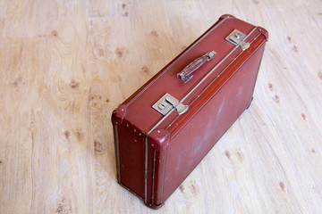 Old leather red suitcase on wooden floor.