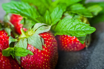 A beautiful ripe fresh strawberry with refreshing mint and sweet powdered sugar on the background of a concrete lid
