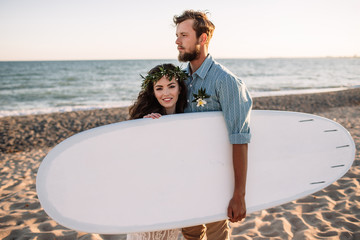 Happy surfers couple standing with surfboards on the sandy beach